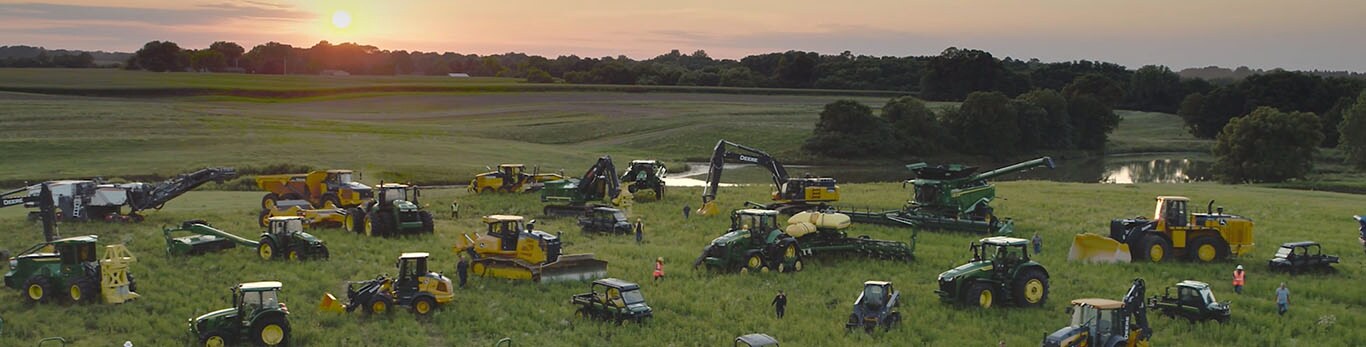 Ihmisiä kävelemässä suurella pellolla erityyppisten John Deere -laitteistojen joukossa.