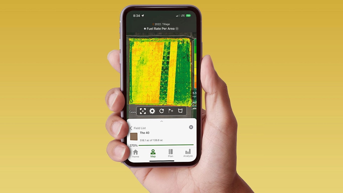 Käsi, joka pitelee älypuhelinta, jossa näkyy John Deere Operations Center ja polttonestetiedot.