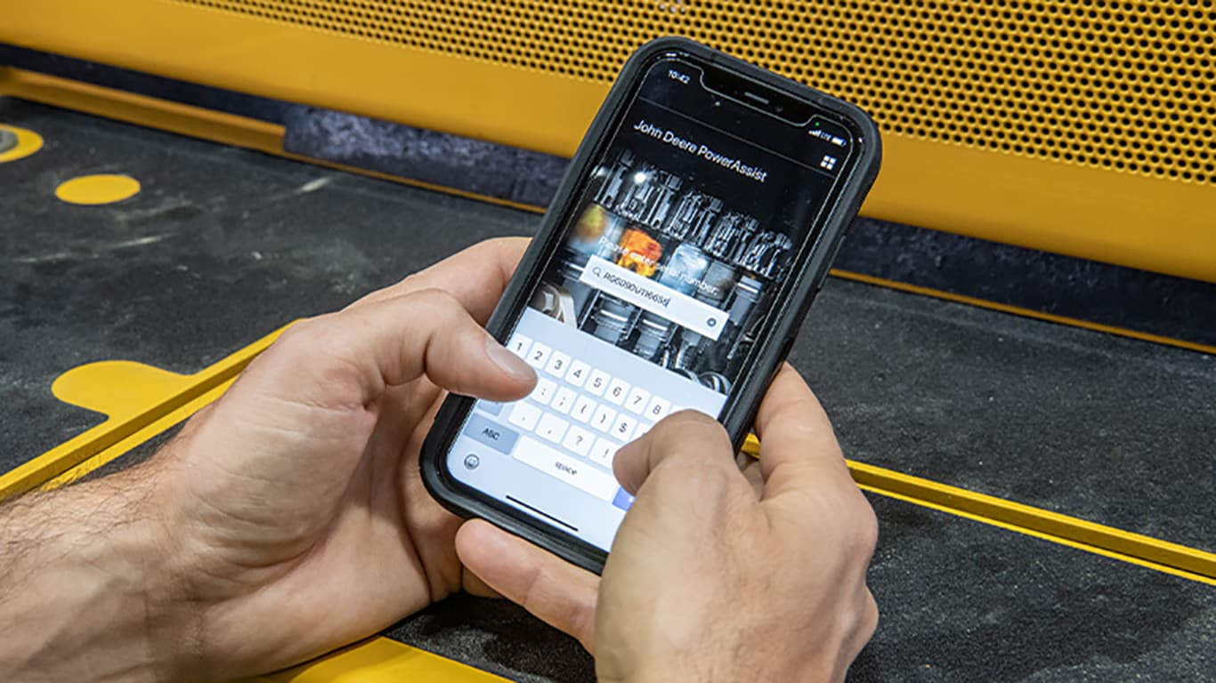Mies, joka hakee älypuhelimella moottorin sarjanumeroa John Deere PowerAssist -sovelluksesta