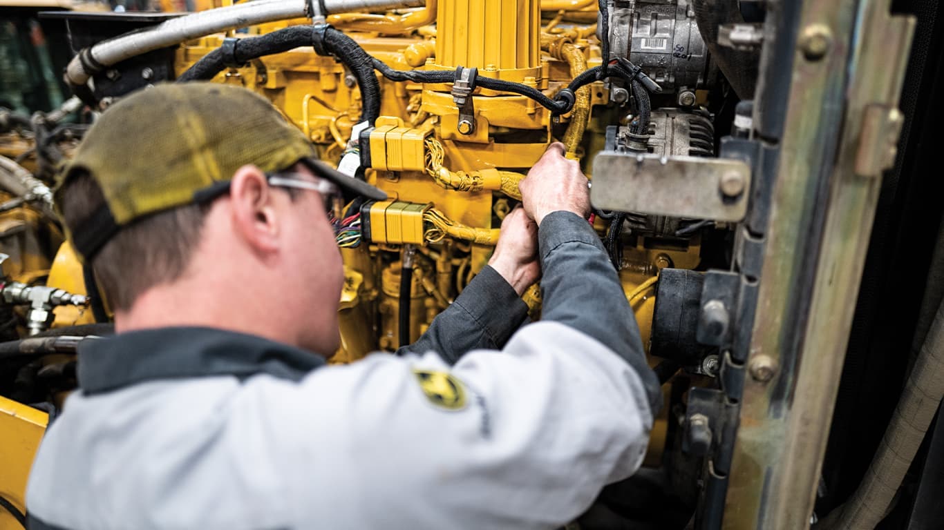 Suojalaseja käyttävä mies, joka työskentelee John Deere -moottorin parissa