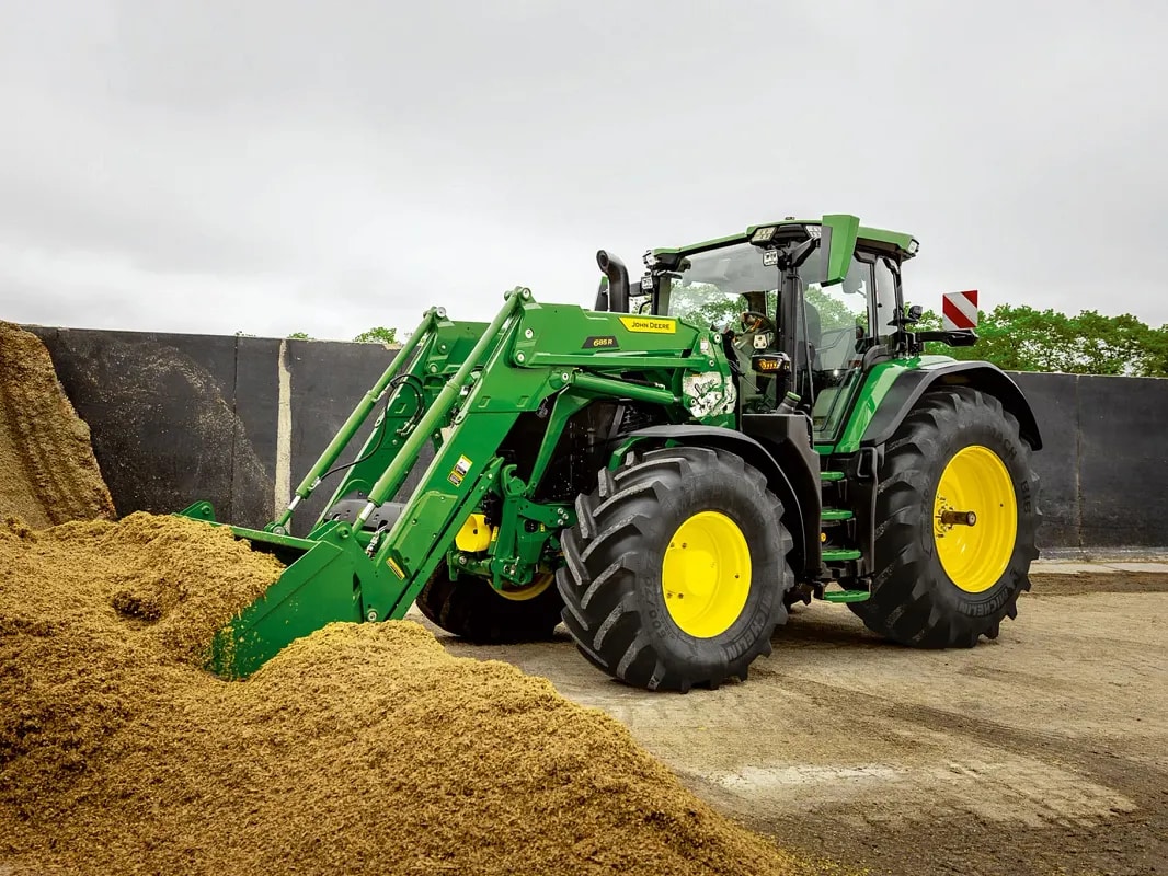 John Deere -traktorin etukuormaimen kauha työntymässä säilörehukasaan maatilaympäristössä.