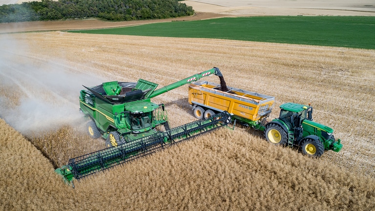 John Deere X-sarjan leikkuupuimuri tyhjent&auml;&auml; rapsinsiemeni&auml; John Deere -traktorin vet&auml;m&auml;&auml;n viljak&auml;rryyn