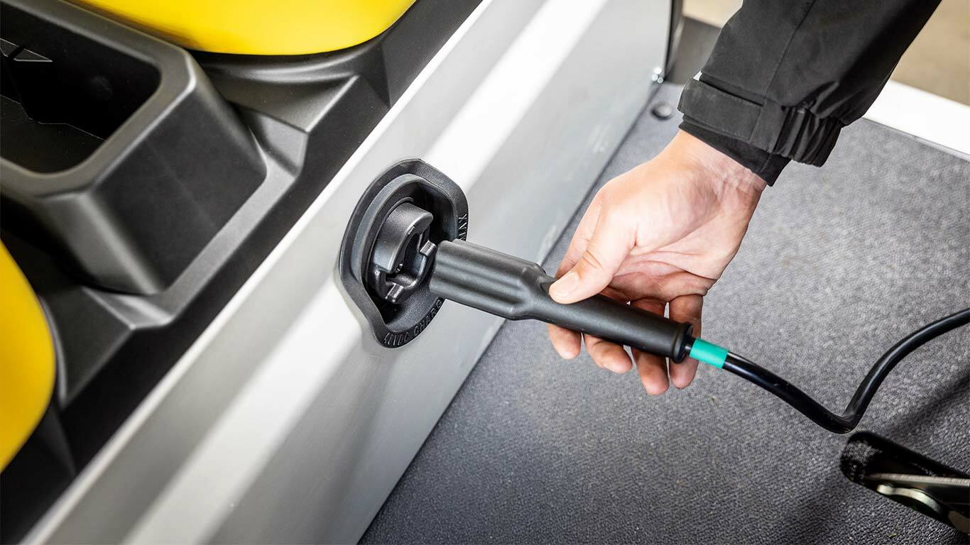 Käsi kytkemässä latausjohtoa sähkökäyttöisen John Deere Gator GS -lava-ajoneuvon sivuliitäntään.