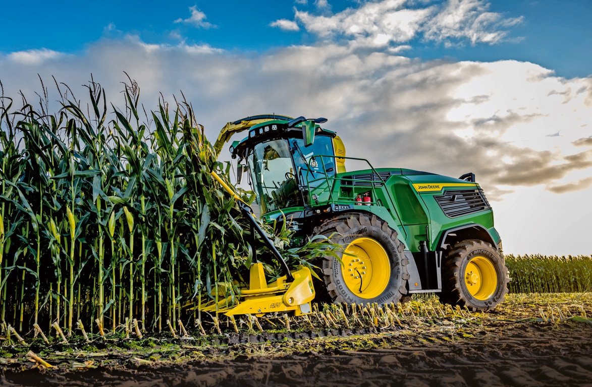 John Deere -ajosilppuri korjaa maissia pellolla sinisen ja pilvisen taivaan alla.