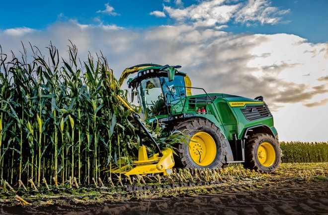 John Deere -ajosilppuri korjaa maissia pellolla sinisen ja pilvisen taivaan alla.