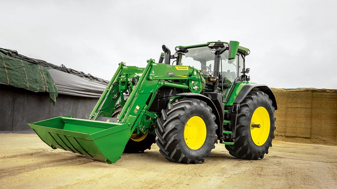 John Deere -traktori, jossa on etukuormain, pysäköitynä maatilalla säilörehuvaraston lähellä.