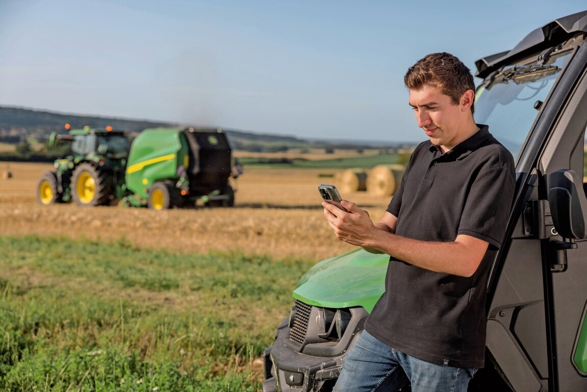 Henkilö tarkistaa paalin dokumentointitiedot matkapuhelimesta, ja taustalla on John Deere VR -paalain