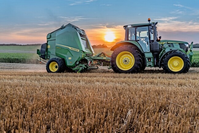 John Deere 6M 150 -traktorin vetämä John Deere V462M olkipellolla auringonlaskun aikaan