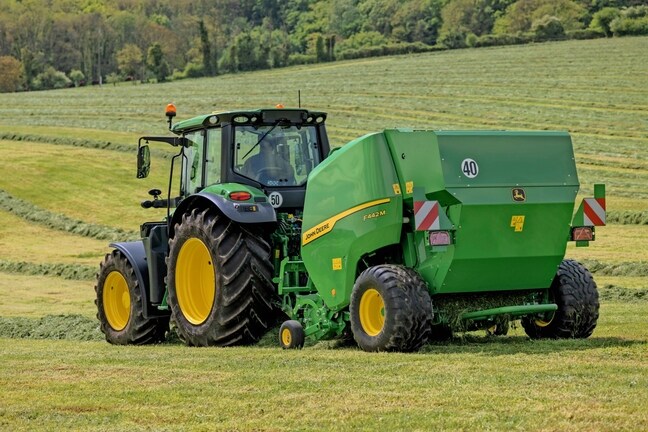 John Deere 6M -traktorin vetämä John Deere F442M -paalain mäkisellä heinäpellolla