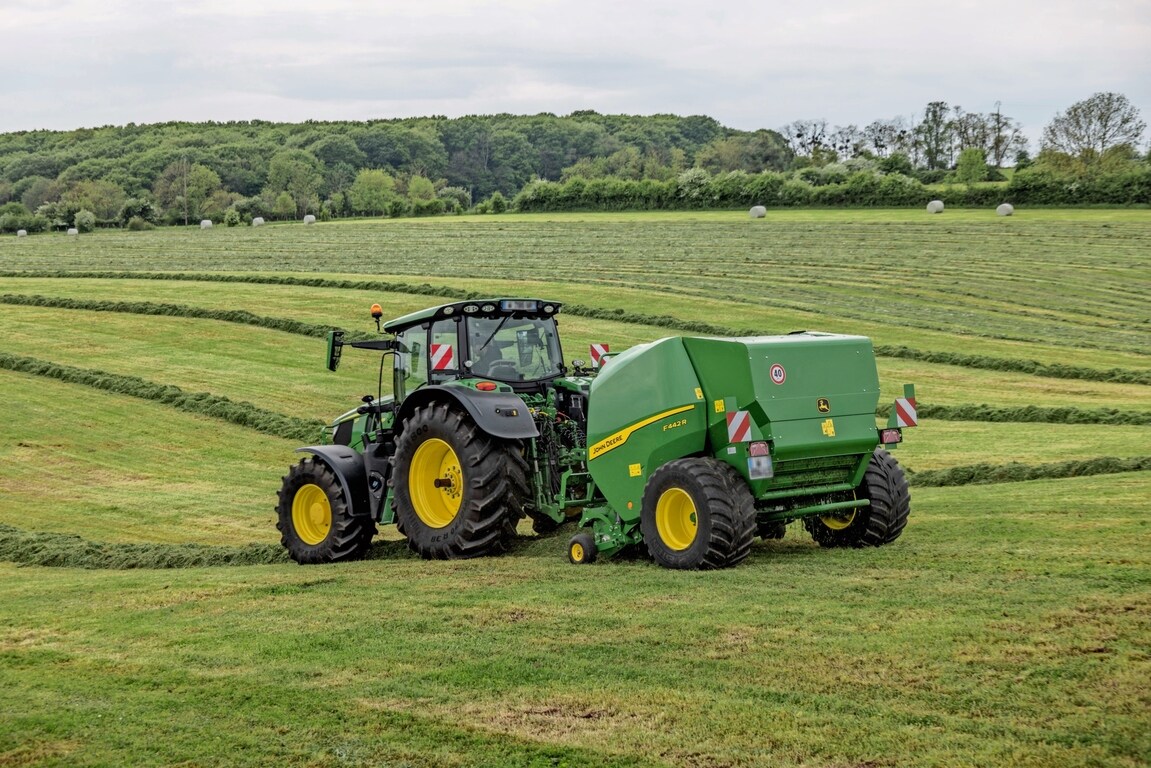 John Deere 6M -traktorin vetämä John Deere F442R -paalain mäkisellä heinäpellolla